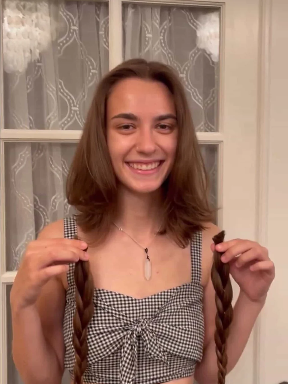 After: a fresh shoulder-length cut, smiling with the two donated braids in hand.