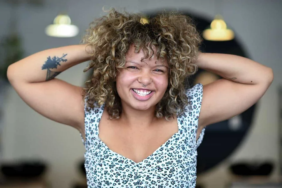 Tycetycehair grinning with both hands lifted into her curls, in the salon.