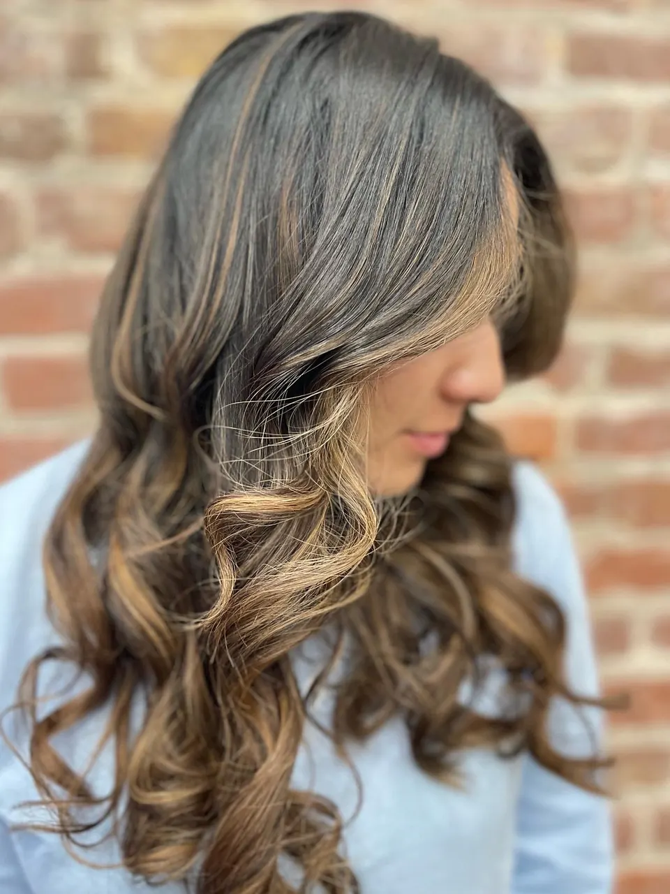 Warm caramel highlights through long brunette hair, curled through the ends.