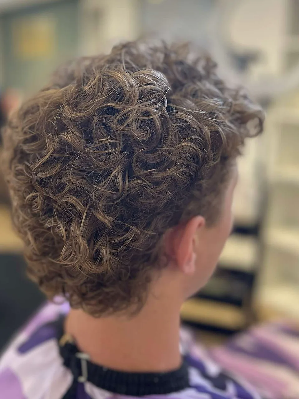 A curly mullet with tapered sides and defined curl through the top and nape.